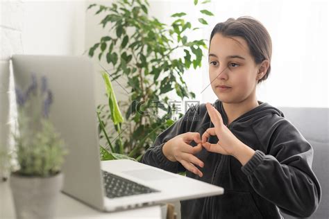 微笑的少女聋哑残疾儿童女学生在笔记本电脑上学习在线课程，通过视频电话会议与老师交流，在虚拟课程中使用手语显示手势。高清摄影大图-千库网