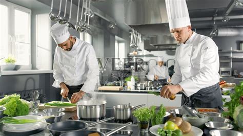 两个著名的厨师在一个大餐厅的厨房团队工作。蔬菜和配料无处不在，厨房看起来很现代，有很多不锈钢。照片摄影图片_ID:307937978-Veer图库
